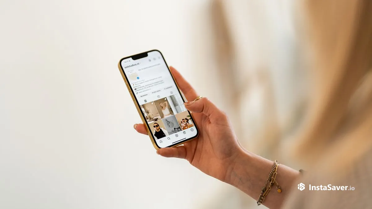 A hand holding a phone showing an Instagram profile and post grid