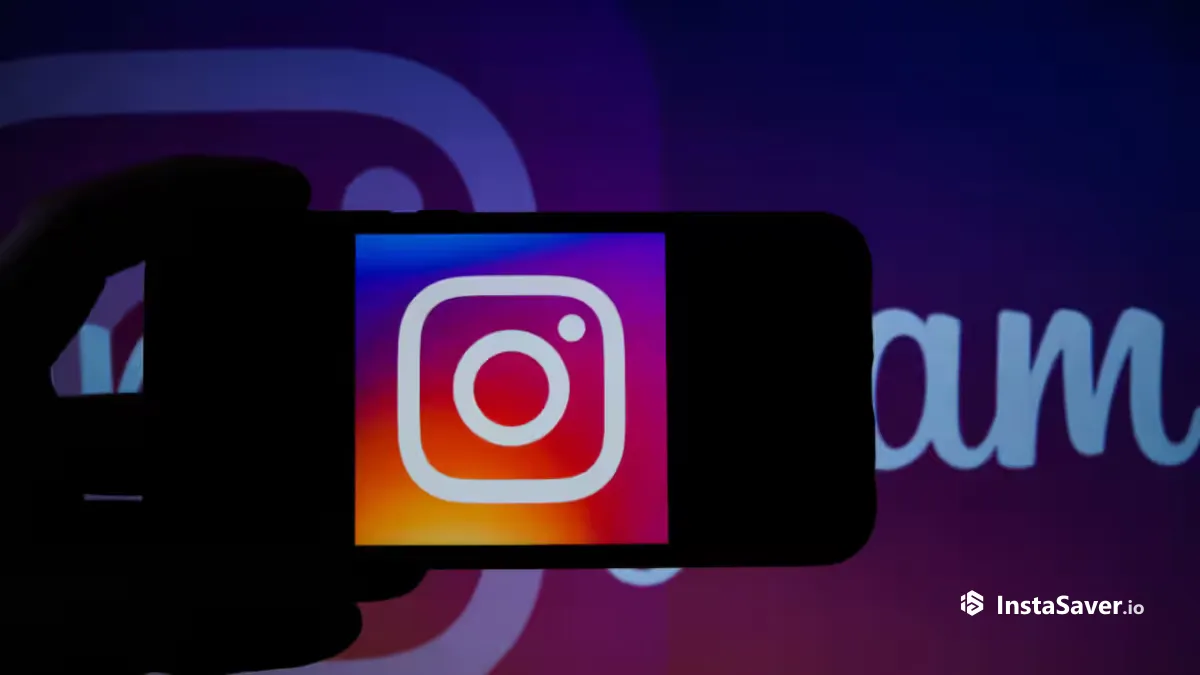 A hand holding a phone showing the Instagram logo in front of a large Instagram sign
